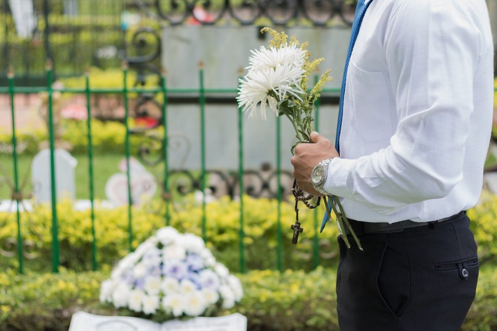 Man holding flowers over a grave.